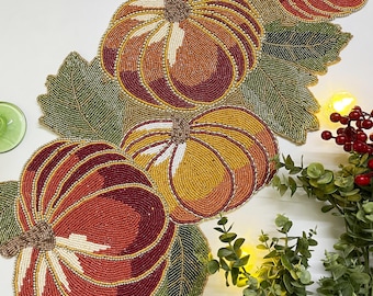 May include: A beaded table runner with a fall theme featuring pumpkins and leaves in shades of orange, red, green, and gold.