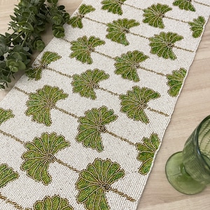 Peut inclure: Un chemin de table blanc perlé avec un motif floral vert. Le chemin de table est fait de petites perles rondes cousues ensemble pour créer un design délicat et complexe.