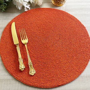 Peut inclure: Un set de table rond en perles orange avec une fourchette et un couteau dorés dessus.
