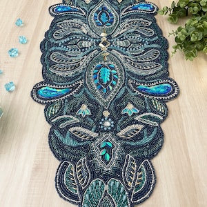 Puede incluir: Un camino de mesa de cuentas con un dise&ntilde;o de paisley en tonos de azul verdoso, azul y dorado. El camino de mesa est&aacute; hecho de peque&ntilde;as cuentas y lentejuelas, creando un efecto brillante.