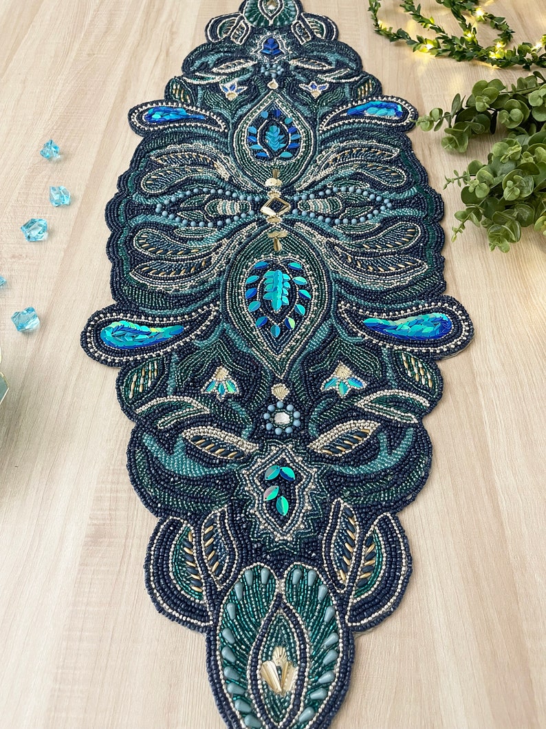 Puede incluir: Un camino de mesa de cuentas con un dise&ntilde;o de paisley en tonos de azul verdoso, azul y dorado. El camino de mesa est&aacute; hecho de peque&ntilde;as cuentas y lentejuelas, creando un efecto brillante.