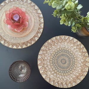 Könnte beinhalten: Zwei goldene und weiße Perlen-Platzsets mit komplizierten Designs. Ein Platzset hat eine rosa Blume in der Mitte.