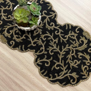 May include: Black beaded table runner with a gold floral design. The runner has a scalloped edge and is perfect for adding a touch of elegance to any table.