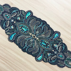 Puede incluir: Un camino de mesa de cuentas con un dise&ntilde;o de paisley en tonos de turquesa, verde y negro. El camino de mesa est&aacute; decorado con detalles dorados y cuentas iridiscentes.