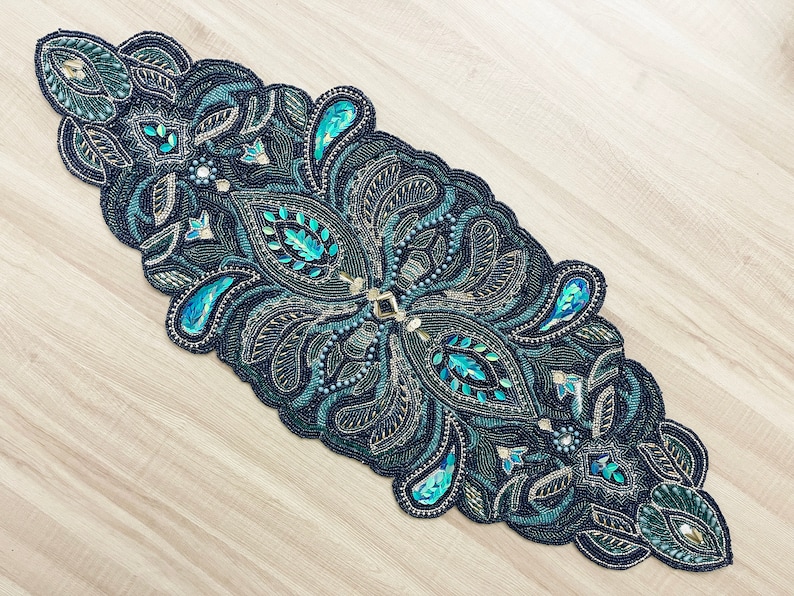 Puede incluir: Un camino de mesa de cuentas con un dise&ntilde;o de paisley en tonos de turquesa, verde y negro. El camino de mesa est&aacute; decorado con detalles dorados y cuentas iridiscentes.