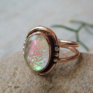 May include: A copper ring with a double band and a large oval iridescent opal-like stone set in the center. The stone has a pink, green, and white color.