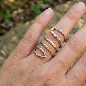 Peut inclure: Une bague en spirale de couleur cuivre avec un design en bobine continue qui s'enroule autour du doigt. La surface métallique est texturée avec un motif répétitif en forme de losange sur toute la longueur de l'anneau, créant un aspect uniforme.