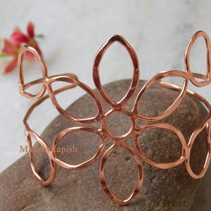 May include: A copper flower-shaped bangle bracelet. The bracelet is made of thin, hammered copper wire and has a delicate, openwork design.