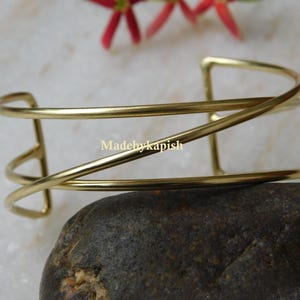 May include: A gold-toned metal bangle bracelet with a simple, geometric design. The bracelet is made of three thin bands of metal that are interwoven to create a unique and modern look.