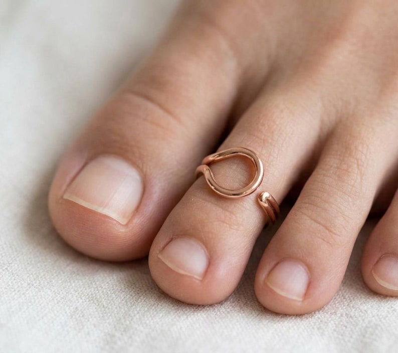 Op de afbeelding: Een open teenring in ros&eacute;goudkleur met een glad, cirkelvormig ontwerp. De ring is vervaardigd met een gepolijste metalen afwerking en heeft een verstelbare opening, waardoor deze comfortabel om de teen kan worden gedragen voor een strakke look.