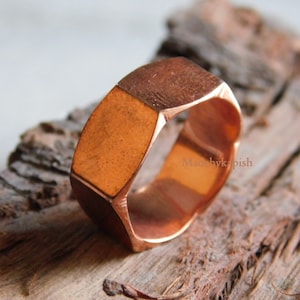 May include: A copper ring with a hexagonal shape. The ring is made from a single piece of metal and has a smooth, polished finish.