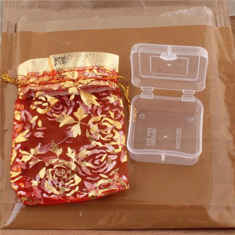 May include: A red and gold floral drawstring bag and a clear plastic box with the word "CHARMBOX" printed on it.