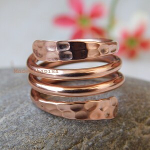 May include: A hammered copper ring with a spiral design. The ring is made of three bands of copper that are twisted together.