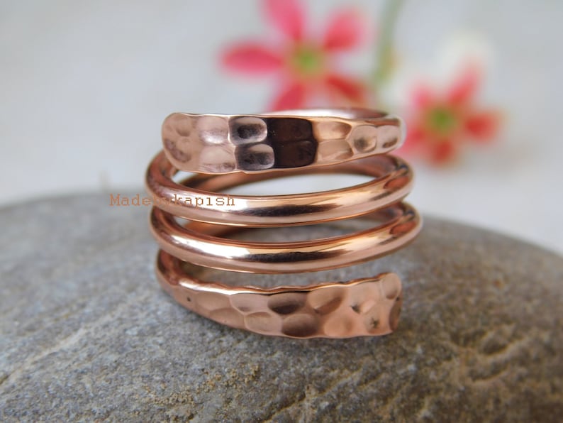 May include: A hammered copper ring with a spiral design. The ring is made of three bands of copper that are twisted together.