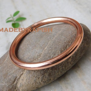 Könnte beinhalten: Ein schlichtes Kupferarmband, ein traditionelles Schmuckstück, das auf einem grauen Stein liegt.