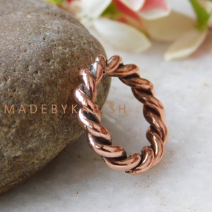 May include: A copper-colored ring with a twisted rope design. The ring is made of metal and has a smooth, polished finish.