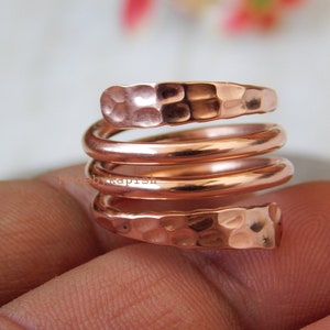 May include: A copper ring with a hammered finish, coiled into a spiral shape. The ring is worn on a finger.