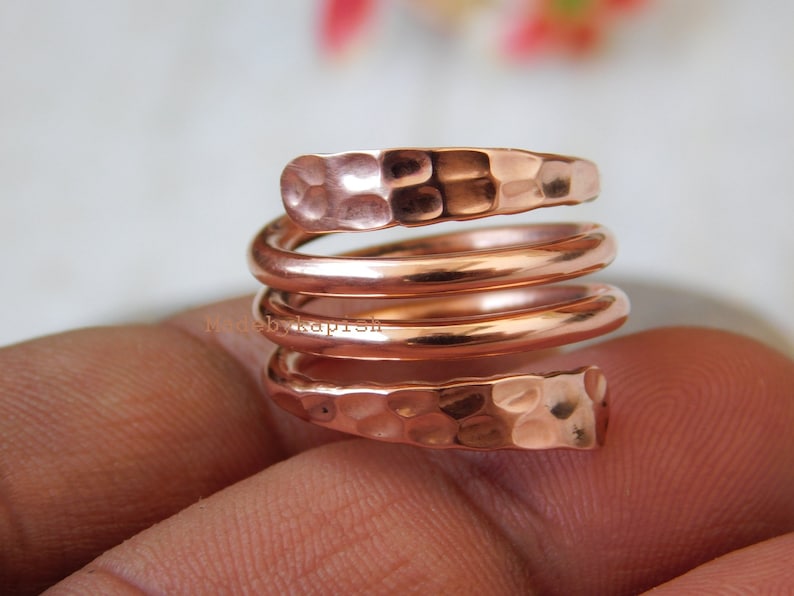 May include: A copper ring with a hammered finish, coiled into a spiral shape. The ring is worn on a finger.