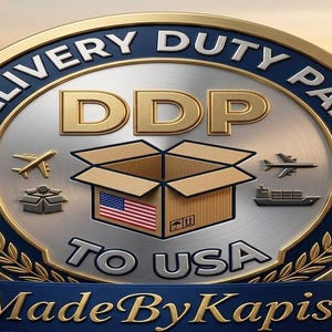 Puede incluir: Un emblema met&aacute;lico circular con borde dorado y centro plateado que presenta el texto DELIVERY DUTY PAID DDP TO USA. El dise&ntilde;o incluye una caja de cart&oacute;n con una bandera de EE. UU., iconos de aviones y un barco, y el texto MadeByKapish en una cinta azul.