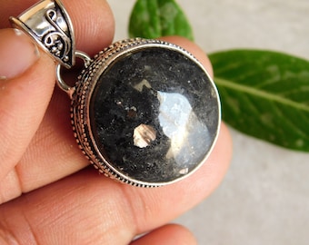 May include: A silver pendant with a round black stone with gold flecks. The pendant has a decorative bail.