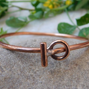 May include: A copper bangle bracelet with a simple, minimalist design. The bracelet features a single, rounded, copper clasp.