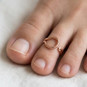 Op de afbeelding: Een open teenring in ros&eacute;goudkleur met een glad, cirkelvormig ontwerp. De ring is vervaardigd met een gepolijste metalen afwerking en heeft een verstelbare opening, waardoor deze comfortabel om de teen kan worden gedragen voor een strakke look.