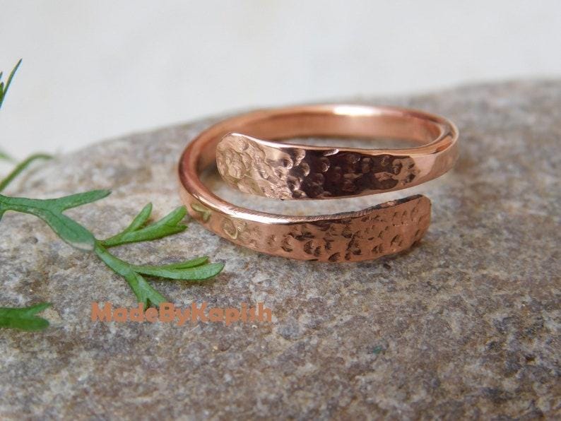 May include: A copper bypass ring featuring a hammered, textured finish on the outer surface. The band is open-ended, allowing for adjustable sizing, and displays a warm, metallic reddish-brown tone. The text MadeByKapish is visible.