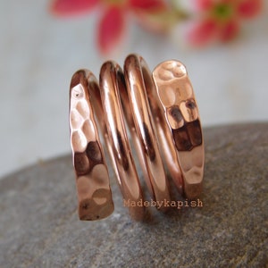 May include: A hammered copper ring with a spiral design. The ring is made of multiple bands of copper that are twisted together. The ring is a warm copper colour and has a rustic look.