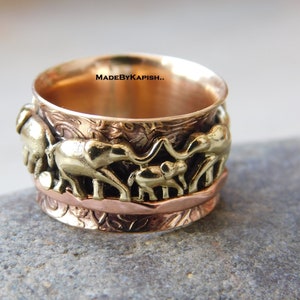 May include: A spinning ring with a design of elephants in gold and copper tones. The ring is made of metal and has a textured surface. The text "MADEBYKAPISH." is visible on the ring.