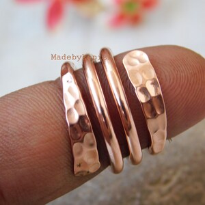 May include: A set of four hammered copper rings stacked on a finger. The rings are a warm copper colour and have a textured, hammered finish.