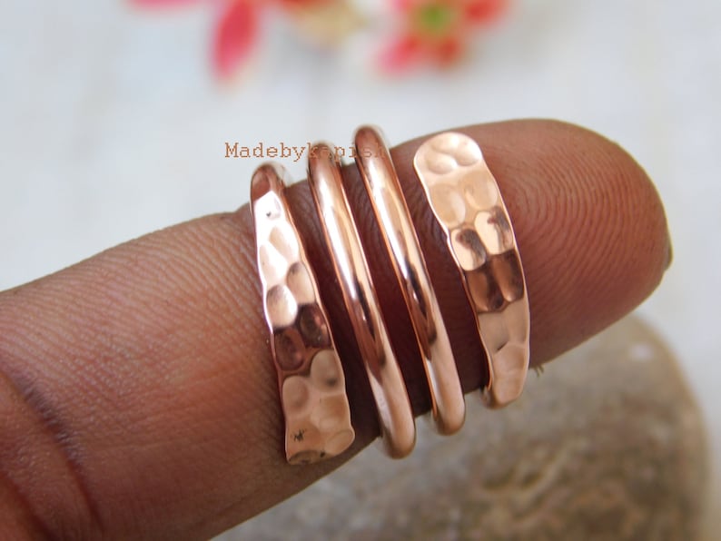 May include: A set of four hammered copper rings stacked on a finger. The rings are a warm copper colour and have a textured, hammered finish.