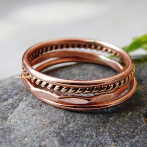May include: Set of three copper rings, one with a twisted rope design, one with a hammered finish, and one with a smooth, polished finish.