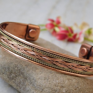 Puede incluir: Una pulsera magnética de cobre con un diseño trenzado de alambre de cobre y latón. La pulsera tiene un cierre magnético.