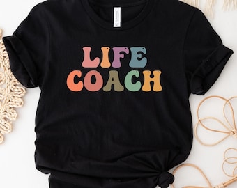 May include: Black t-shirt with the text "LIFE COACH" in rainbow colored letters.