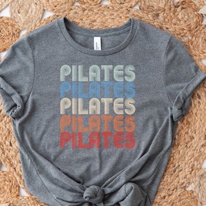 May include: A gray t-shirt with the word "PILATES" repeated five times in a retro rainbow design.