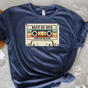 May include: A navy blue t-shirt with a vintage cassette tape graphic. The tape has the text "Best of 1976 Limited Edition" printed on it.