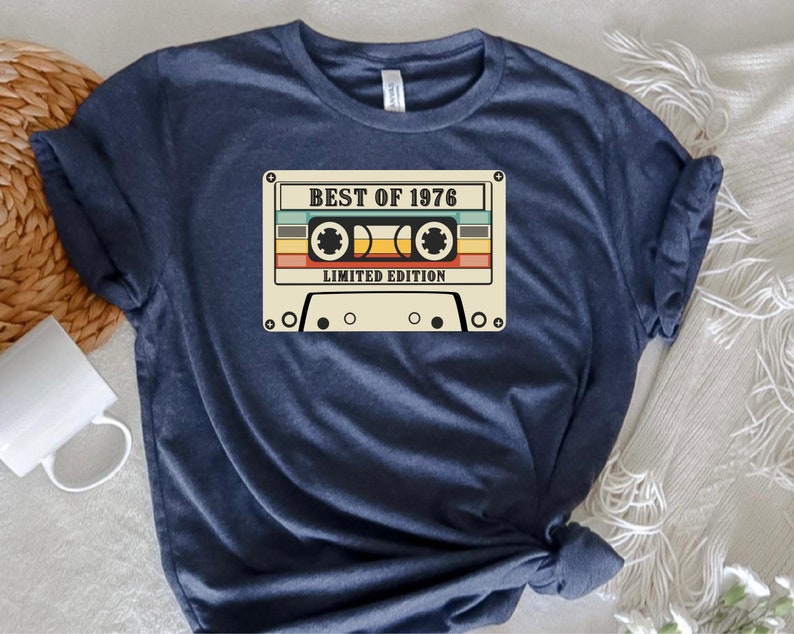 May include: A navy blue t-shirt with a vintage cassette tape graphic. The tape has the text "Best of 1976 Limited Edition" printed on it.