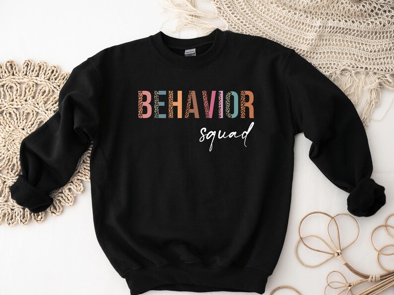 May include: Black sweatshirt with the text "BEHAVIOR squad" in colorful letters with a leopard print pattern.