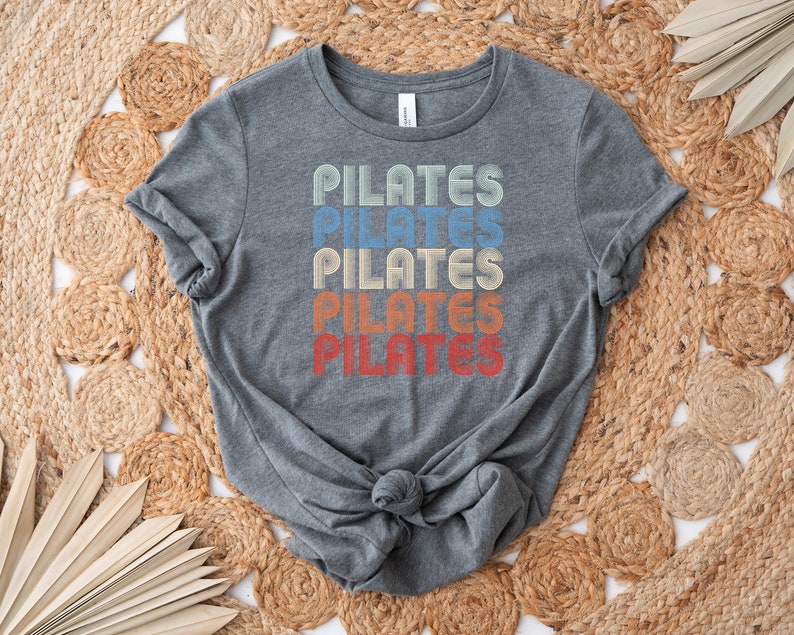 May include: A gray t-shirt with the word "PILATES" repeated five times in a retro rainbow design.