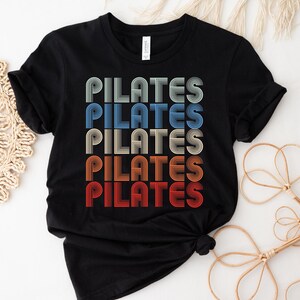 May include: Black t-shirt with the word "PILATES" repeated five times in a retro, rainbow-colored font.