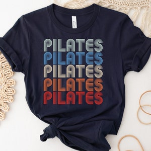 May include: A navy blue t-shirt with the word "PILATES" repeated five times in a retro, multi-colored font.
