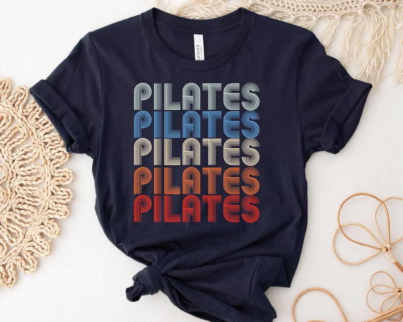 May include: A navy blue t-shirt with the word "PILATES" repeated five times in a retro, multi-colored font.