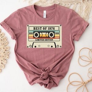 May include: A mauve t-shirt with a vintage cassette tape graphic. The tape has the text "Best of 1976 Limited Edition".