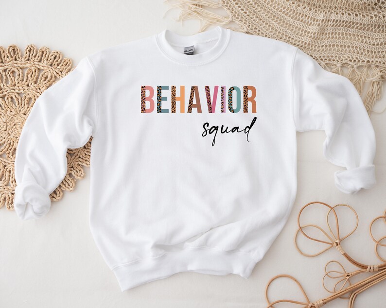 May include: White sweatshirt with the text "BEHAVIOR squad" in colorful letters with a leopard print pattern.