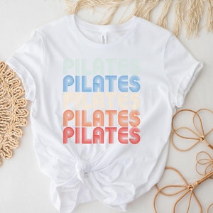 May include: White t-shirt with the word "PILATES" repeated four times in a retro, rainbow-colored font.