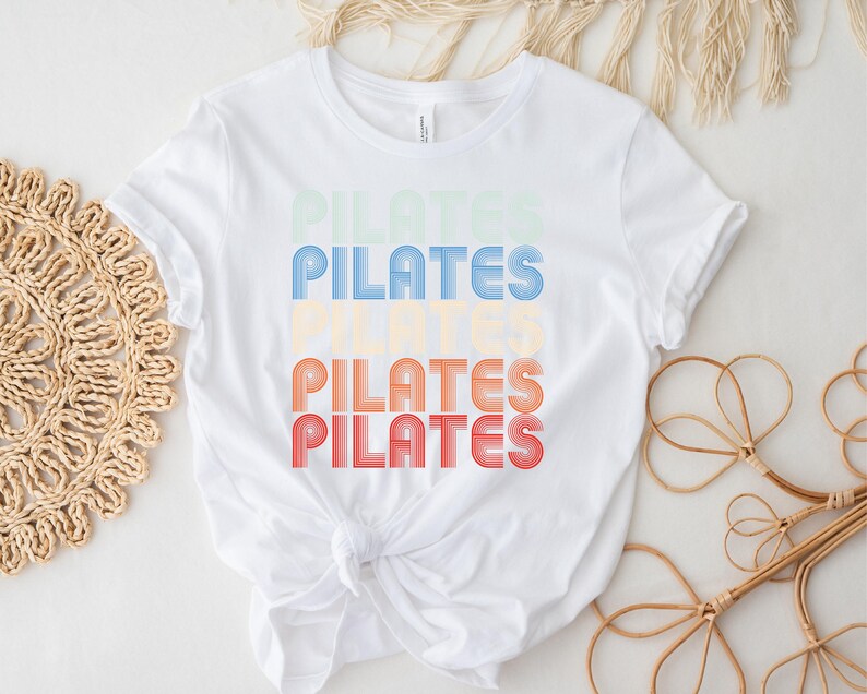 May include: White t-shirt with the word "PILATES" repeated four times in a retro, rainbow-colored font.