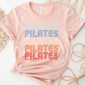 May include: A pink t-shirt with the word "PILATES" repeated four times in a retro, rainbow-colored font.
