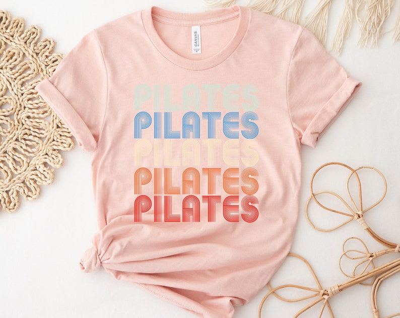 May include: A pink t-shirt with the word "PILATES" repeated four times in a retro, rainbow-colored font.
