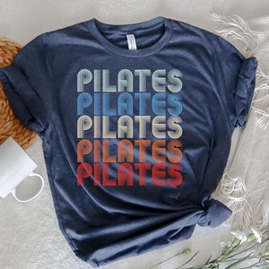 May include: A navy blue t-shirt with the word "PILATES" repeated five times in a retro, rainbow-colored font.