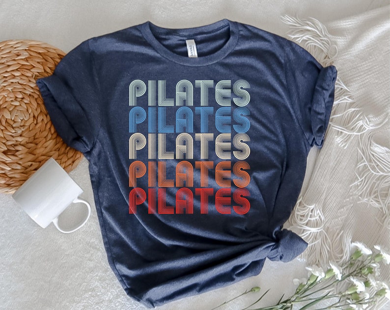 May include: A navy blue t-shirt with the word "PILATES" repeated five times in a retro, rainbow-colored font.